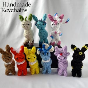 May include: A collection of handmade crochet keychains in various colors, including brown, orange, yellow, blue, purple, black, white, and green. The keychains are in the shape of a cartoon animal with large ears. The text "Handmade Keychains" is at the top.