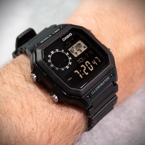 May include: Black digital Casio watch with a square face, displaying the time 7:20:47. The watch has a world map icon and the word "ILLUMINATOR". The watch is on a black band.