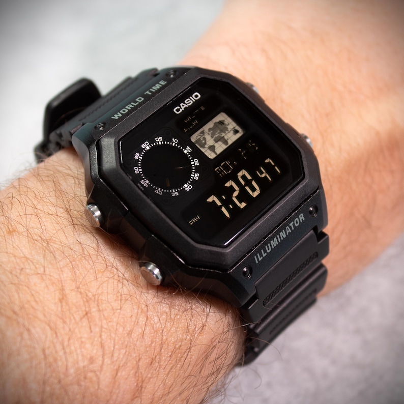 May include: Black digital Casio watch with a square face, displaying the time 7:20:47. The watch has a world map icon and the word "ILLUMINATOR". The watch is on a black band.