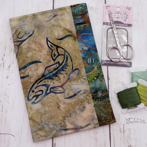 May include: A rectangular fabric case featuring a batik-style fish pattern in shades of olive, tan, and blue. Beside the case are a package of Sew-Ology needles and three small spools of green embroidery thread in varying shades of olive and lime.