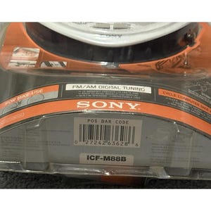 Pu&ograve; includere: Una nuova radio per bici con computer di bordo e sintonizzazione digitale Sony ICF-M88B FM/AM, confezionata in una custodia di plastica trasparente. La confezione presenta accenti arancioni e neri con il logo Sony e informazioni sul prodotto. La radio &egrave; progettata per l'uso in bicicletta.