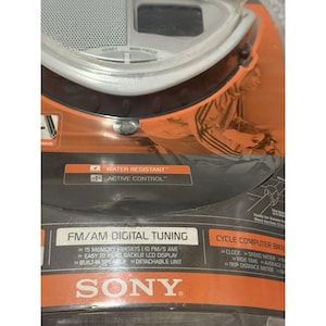 Pu&ograve; includere: Una nuova radio per computer da bicicletta Sony, confezionata in arancione e nero. Include sintonizzazione digitale FM/AM, 15 preimpostazioni di memoria, un display LCD retroilluminato e un altoparlante integrato. La confezione evidenzia anche la resistenza all'acqua e il controllo attivo.