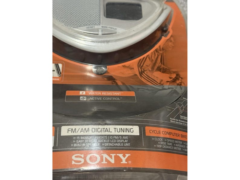 Pu&ograve; includere: Una nuova radio per computer da bicicletta Sony, confezionata in arancione e nero. Include sintonizzazione digitale FM/AM, 15 preimpostazioni di memoria, un display LCD retroilluminato e un altoparlante integrato. La confezione evidenzia anche la resistenza all'acqua e il controllo attivo.