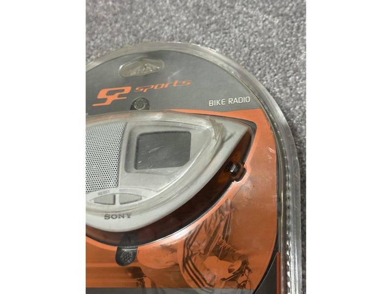 Pu&ograve; includere: Una radio per bici Sony argento e nera nella sua confezione originale. La radio ha un piccolo schermo, un altoparlante e pulsanti di controllo. La confezione riporta "SP Sports" e "Bike Radio".