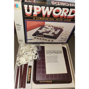 May include: An open box set of the Upwords 3-dimensional word game. The box features the game title in large, colorful letters. Inside, the game board, letter tiles, and instructions are visible. The game is designed for ages 10 and up.