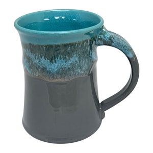 May include: A teal and black ceramic mug with a flared base and a wide handle. The mug has a mottled glaze with shades of blue and green.