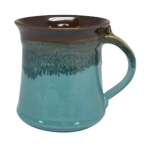 May include: A teal ceramic mug with a brown rim and handle. The mug has a mottled glaze with a brown and green pattern.