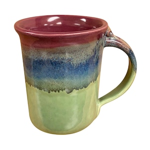 May include: A ceramic mug featuring a multi-colored glaze with a deep maroon rim, a central band of dark blue, and a light green base. The mug has a curved handle on the right side and a smooth, glossy finish throughout the exterior surface.