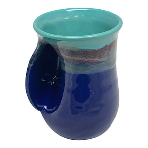 May include: A blue and turquoise ceramic mug with a unique handle that wraps around the side. The mug has a glossy finish and a hand-painted design.