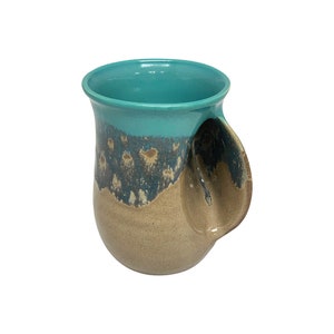 May include: A teal and brown ceramic mug with a unique handle that is part of the mug itself. The handle is a loop that is integrated into the side of the mug.