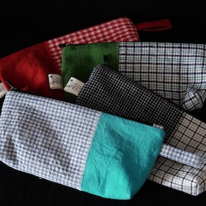 Peut inclure: Plusieurs pochettes zippées faites à la main, aux couleurs et motifs variés. Les pochettes présentent des tissus à carreaux rouges, verts, noirs et blancs, à carreaux bleus et blancs et turquoise. Chaque pochette a une petite boucle en tissu.