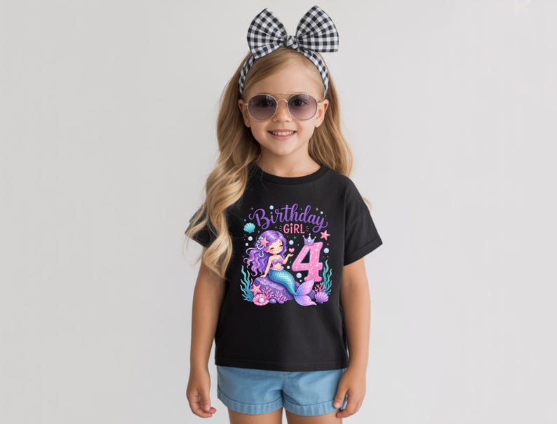 May include: A black short-sleeved t-shirt featuring a graphic of a purple-haired mermaid sitting on a rock, the number 4, and the text Birthday GIRL. The design includes sea elements like shells, starfish, and seaweed in pink and blue tones.