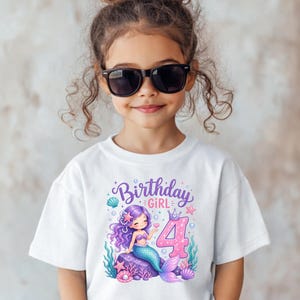 May include: A white short-sleeved t-shirt featuring a graphic print of a purple-haired mermaid sitting on a rock. The design includes the text Birthday GIRL and a large pink number 4, surrounded by colorful seashells, starfish, and bubbles.