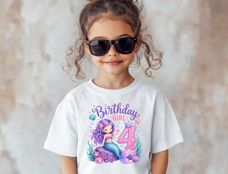 May include: A white short-sleeved t-shirt featuring a graphic print of a purple-haired mermaid sitting on a rock. The design includes the text Birthday GIRL and a large pink number 4, surrounded by colorful seashells, starfish, and bubbles.
