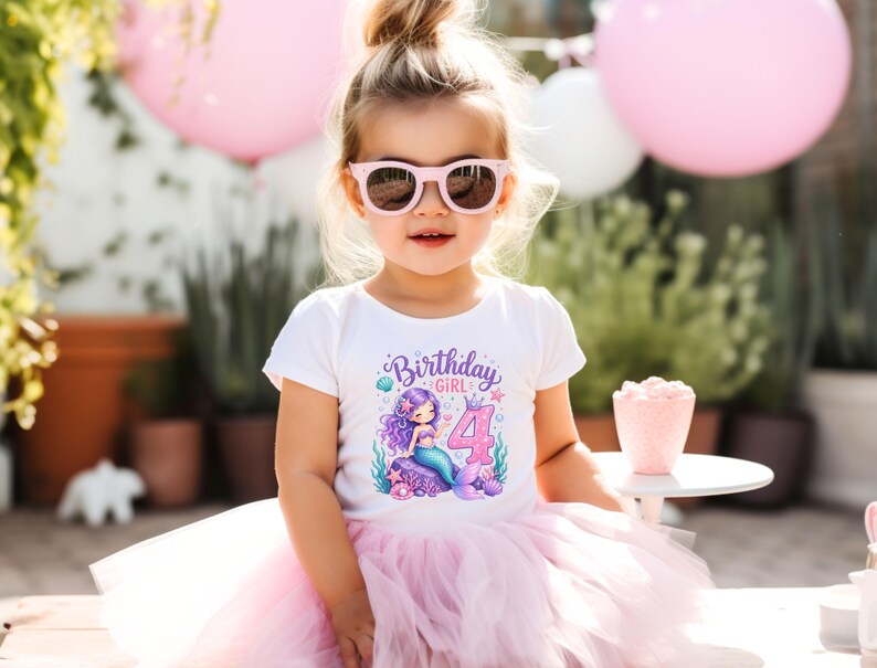 May include: A white short-sleeved t-shirt featuring a graphic of a purple-haired mermaid sitting on a rock next to the number 4 and the text Birthday Girl, paired with a light pink layered tulle tutu skirt and pink-framed sunglasses.