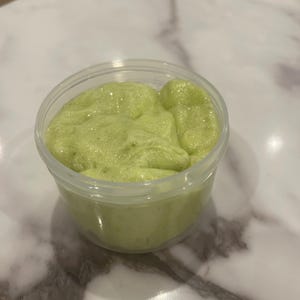Puede incluir: Un recipiente de plástico transparente lleno de slime verde claro con una textura espumosa.