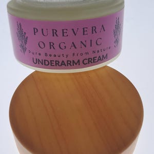 Puede incluir: Un tarro de crema para axilas Purevera Organic con tapa de madera. El tarro tiene una etiqueta rosa con el nombre de la marca y las palabras "Pure Beauty From Nature". La crema est&aacute; en un tarro de cristal transparente.