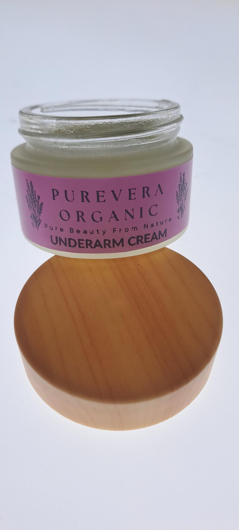 Puede incluir: Un tarro de crema para axilas Purevera Organic con tapa de madera. El tarro tiene una etiqueta rosa con el nombre de la marca y las palabras "Pure Beauty From Nature". La crema est&aacute; en un tarro de cristal transparente.