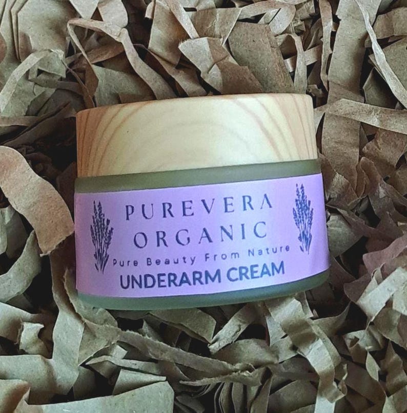Puede incluir: Un peque&ntilde;o frasco de crema para axilas Purevera Organic con tapa de madera y etiqueta morada. La etiqueta presenta el nombre de la marca, la descripci&oacute;n del producto e ilustraciones de lavanda. El frasco est&aacute; rodeado de papel marr&oacute;n.