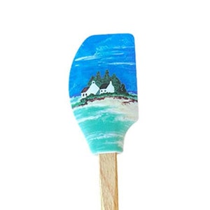 May include: A blue and green silicone spatula with a wooden handle. The spatula has a painted design of a beach scene with two houses and trees. The handle is labeled "Knotwood Lane".