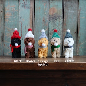 Könnte beinhalten: Fünf Plüschhunde, die Weihnachtsmützen und Schals in verschiedenen Farben tragen: Schwarz, Braun, Orange, Braun und Creme. Die Hunde sind in einer Reihe auf einer Holzoberfläche angeordnet.