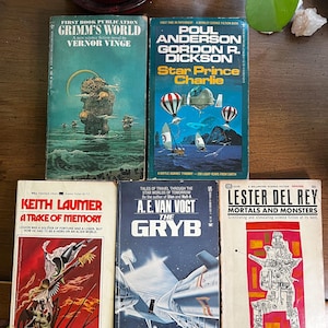 May include: A collection of vintage science fiction paperback books. Titles include "Grimm's World," "Star Prince Charlie," "A Trace of Memory," "The Gryb," and "Mortals and Monsters." The covers feature colorful illustrations of futuristic scenes and characters.