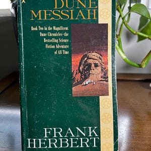 May include: A hardcover book titled "Dune Messiah" by Frank Herbert. The cover is dark green with gold lettering and a desert scene illustration. The book is part of the Dune Chronicles, a science fiction series.