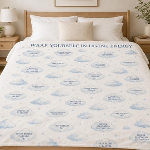 May include: A white fleece blanket featuring a repeating pattern of light blue watercolor clouds and small stars. The text WRAP YOURSELF IN DIVINE ENERGY is printed at the top, with various phrases like DIVINE ENERGY CASCADE, FAST RESULTS, and DEEP SLEEP paired with numerical codes inside the clouds.