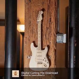 Könnte beinhalten: Eine hellfarbene Holzgitarre ist auf einem strukturierten Holzbalken montiert. Die Gitarre hat ein klassisches Design mit Kopfplatte, Hals, Korpus und Saiten. Das Bild enthält auch den Text "Digital Cutting File Download" und "Created by LaserLuthierCo."