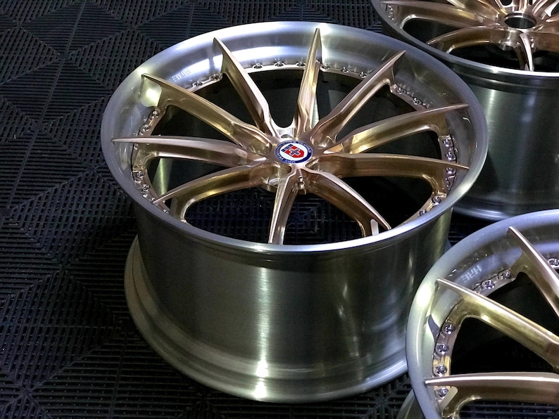 May include: Close-up of three alloy wheels with a multi-spoke design. The wheels have a silver finish with gold-coloured spokes and a central emblem. The wheels are displayed on a black surface.