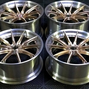 May include: Four alloy wheels with a multi-spoke design. The wheels have a silver rim and a bronze-coloured centre. The wheels are displayed on a dark surface.