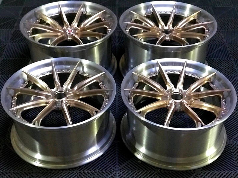May include: Four alloy wheels with a multi-spoke design. The wheels have a silver rim and a bronze-coloured centre. The wheels are displayed on a dark surface.