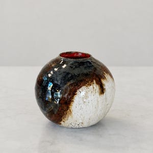 Peut inclure: Un vase sphérique en céramique avec une ouverture étroite, doté d'une finition brillante. L'extérieur présente un mélange de glaçure brun foncé, noire et crème, tandis que le bord intérieur est recouvert d'une glaçure rouge vif et unie.