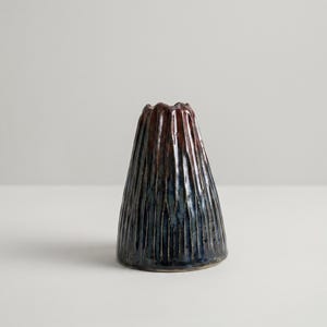 May include: A handmade ceramic vase with a textured, ridged surface. The vase has a conical shape, with a dark blue base that transitions to a reddish-brown rim. The vase is approximately 6 inches tall.