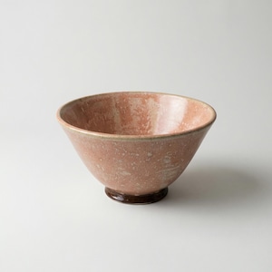 May include: A ceramic bowl with a wide, flared shape and a speckled, reddish-pink glaze. The bowl sits on a small, dark brown base. The interior of the bowl is a lighter shade of pink.