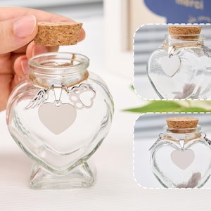 Peut inclure: Un bocal en verre transparent en forme de c&oelig;ur avec un bouchon en li&egrave;ge. Le bocal est orn&eacute; d'un charm argent&eacute; en forme de c&oelig;ur, d'une empreinte de patte et d'une aile. Con&ccedil;u pour contenir des souvenirs.