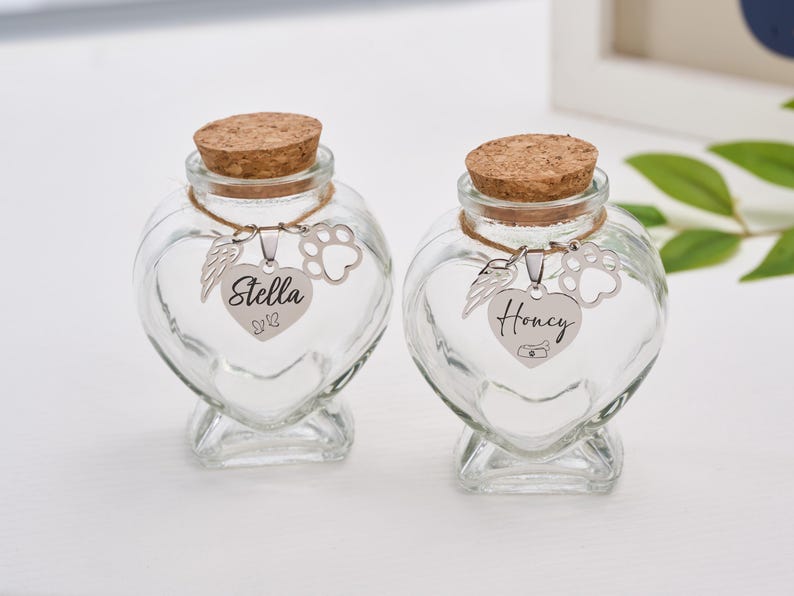 Peut inclure: Deux bocaux en verre transparent en forme de c&oelig;ur avec des bouchons en li&egrave;ge. Chaque bocal a un charm argent&eacute; avec une empreinte de patte, des ailes d'ange et un pendentif en forme de c&oelig;ur avec un nom. On lit "Stella", l'autre "Honey".