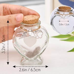 Peut inclure: Un bocal comm&eacute;moratif en forme de c&oelig;ur en verre transparent avec un bouchon en li&egrave;ge. Le bocal mesure 8 cm de haut et 6,5 cm de large. Il poss&egrave;de un charm argent&eacute; avec un c&oelig;ur, une aile et une empreinte de patte. Le bocal contient un peu de fourrure.
