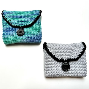 Peut inclure: Deux porte-monnaie en crochet avec une bordure noire et une fermeture à bouton noir. Un porte-monnaie est bleu et vert, l'autre est gris.