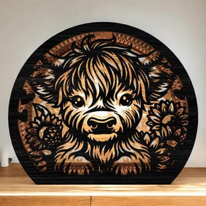 May include: A layered wooden art piece featuring a Highland cow with a fluffy coat and large eyes, surrounded by sunflowers. The artwork is in shades of black and natural wood tones, creating a rustic and charming aesthetic.
