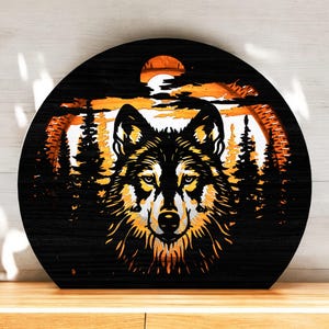 May include: A black, round wooden wall art piece featuring a wolf design. The wolf is centered, with a detailed face and fur in shades of yellow and white. The background depicts a sunset scene with trees and a sun.