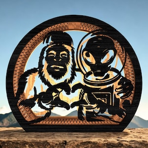 May include: A wooden laser-cut art piece featuring a Bigfoot and an alien forming a heart shape with their hands. The artwork is set within a circular frame with a woven texture, showcasing a whimsical and unique design. The background shows a blue sky and mountains.