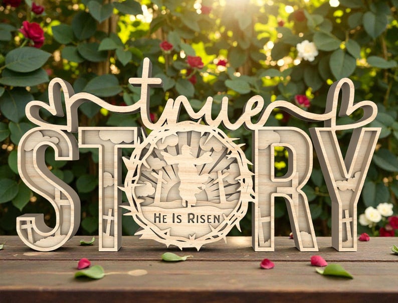May include: Wooden sign with the words "true STORY" in a layered design. The letter "O" features a circular design with a figure and the text "He Is Risen". The sign is set on a wooden surface with a blurred background of greenery and flowers.