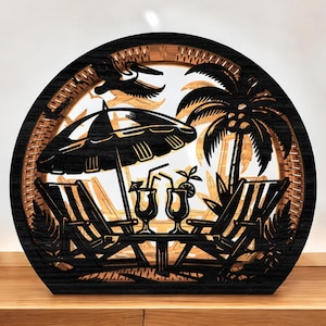 May include: A black and tan wooden beach scene sculpture. The layered design features a palm tree, beach chairs, an umbrella, and cocktails. A pelican is flying overhead. The sculpture is in a round frame.
