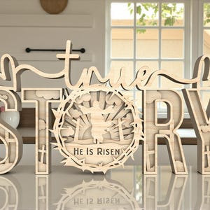 May include: Wooden sign with the words "true STORY" in a layered design. The letter "O" features a circular cutout with a religious scene and the text "He Is Risen". The sign is made of light-colored wood and is displayed on a reflective surface.