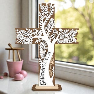 May include: A wooden cross with a tree design cut out of the centre. The cross features the words "Patience, Joy, Kindness, Goodness" and other words. The text "Galatians 5:22-23" is also visible. The cross is brown with a white tree design.