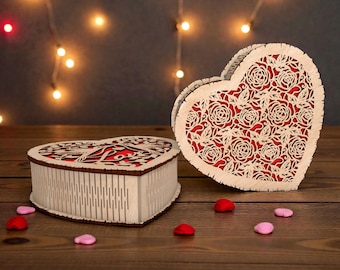 May include: Two heart-shaped wooden boxes with intricate floral cutouts. The boxes are light-colored with a red interior, and the lids feature a delicate rose design. Scattered around are red and pink heart-shaped decorations, suggesting a romantic theme.