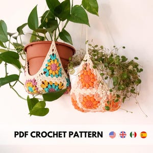 May include: Two crocheted plant hangers with colorful granny square designs. The hangers are made with white yarn and feature bright pink, orange, yellow, and blue accents. The hangers are hanging from the ceiling and are holding potted plants.