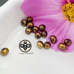 May include: A close-up of a collection of 12 iridescent brown glass beads, scattered on a white surface with a pink flower petal in the background. The beads are round and have a smooth, glossy finish. The beads are perfect for jewelry making or other craft projects.