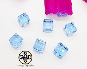 May include: Six light blue square glass beads with a hole in the center. The beads are on a white surface.